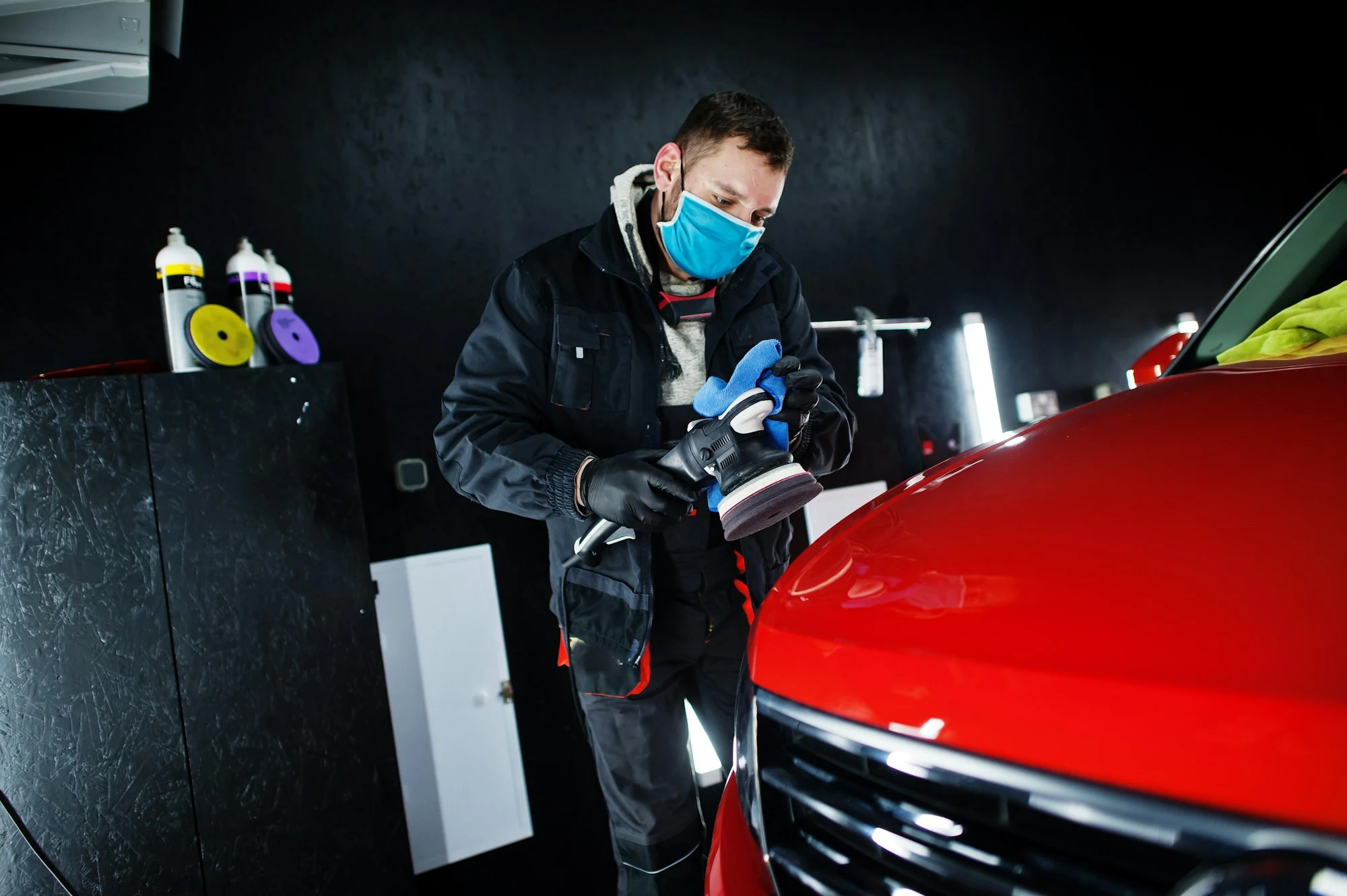 Detailer polishing red SUV hood with orbital buffer for high-gloss paint finish