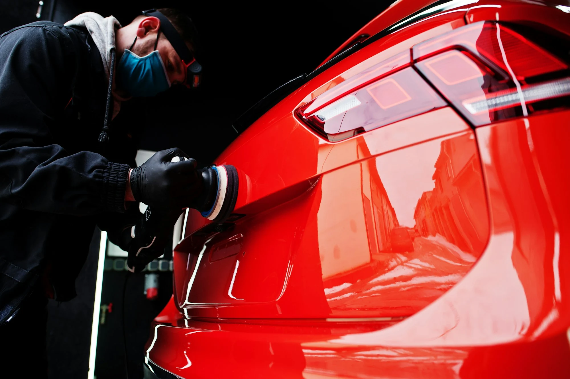 Technician using buffer machine on red car rear paint surface for scratch removal and shine