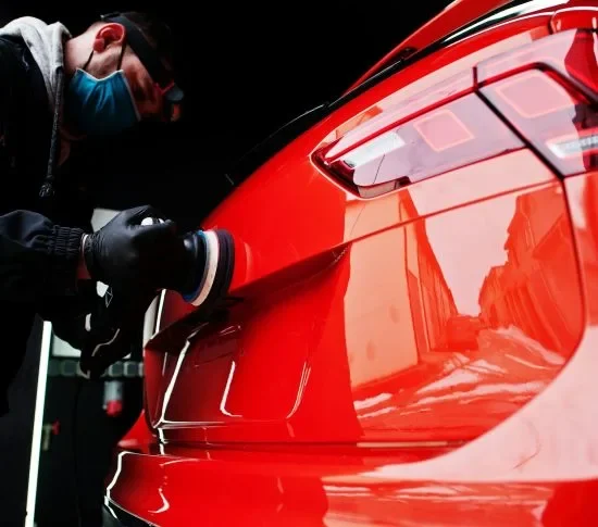 Auto detailer polishing red car rear panel with machine buffer during detailing service package